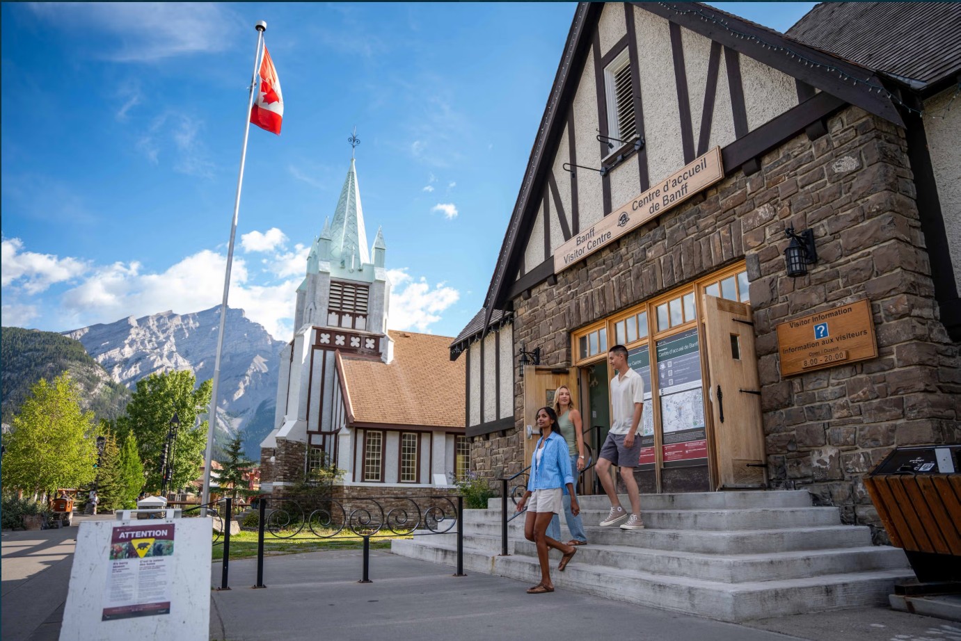 旅行者サイン、中心街の教会、カナダ国旗、山の背景が見えるバンフ・ビジターセンター（Banff Visitor Centre）入口
